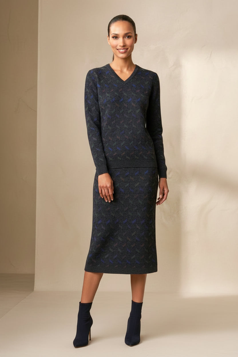 A woman modeling a dark navy blue knit sweater and matching skirt set with a subtle abstract pattern, standing against a neutral beige wall.