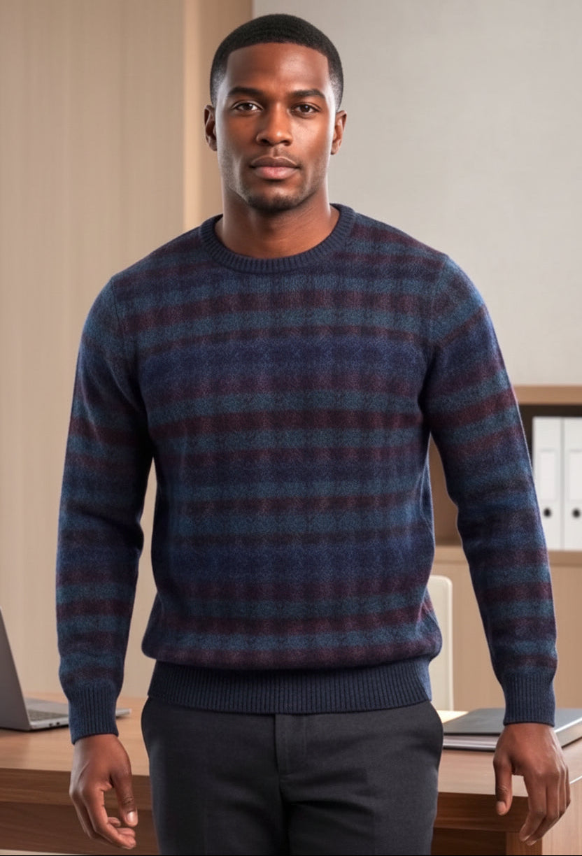 A man wearing a long-sleeve crewneck sweater with a textured plaid pattern in navy blue, purple, and brown, paired with dark gray trousers, standing in front of a bright window.