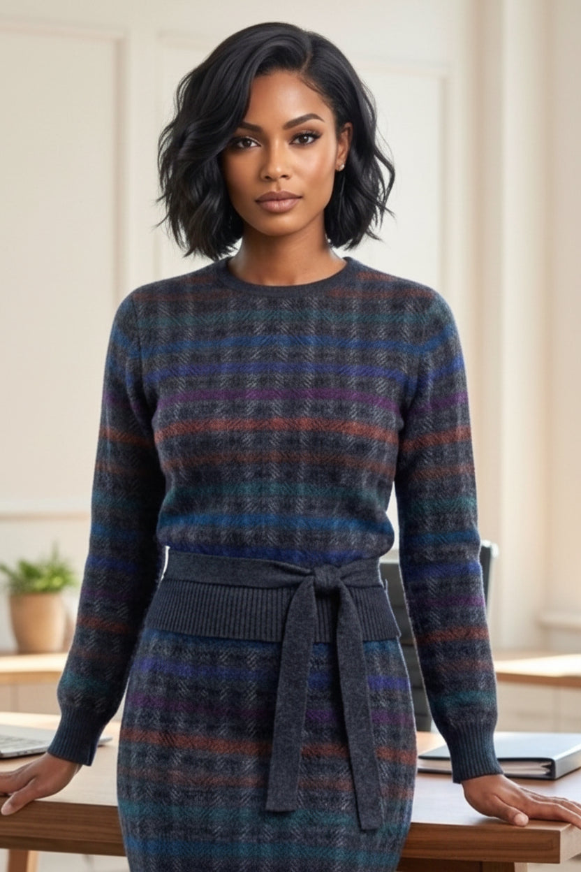 A woman wearing a dark, long-sleeve knit sweater dress with a matching tie belt at the waist. The dress features a textured plaid pattern in shades of navy, blue, purple, and brown.